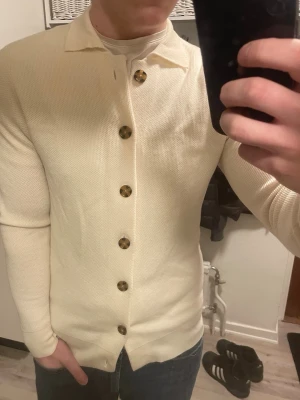 Stickad merinoull cardigan - Otroligt snygg beige stickad merinoull cardigan från John Henric. Passar perfekt till kallare väder. Modellen är 180cm, 75kg. Knappen längst ner saknas. Priset kan såklart diskuteras!