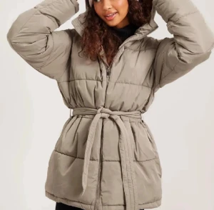 Jacka från Nelly - Säljer en beige pufferjacka med huva och bälte i midjan. Jackan har quiltad design, dragkedja framtill och långa ärmar. Perfekt för dig som vill ha en varm och snygg jacka med loose passform och cool siluett. Fråga gärna om fler bilder eller mått! Priset går att diskuteras💕