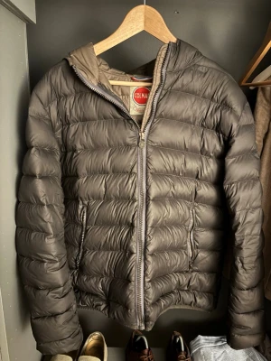 Grå dunjacka från Colmar - Snygg grå dunjacka från Colmar med huva och quiltad design. Jackan har dragkedja framtill och två sidofickor med dragkedja. Perfekt för kyliga dagar och enkel att matcha med olika outfits.