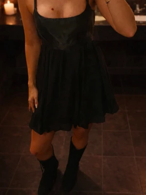 Svart kort klänning med knytband - Säljer en svart kort klänning med tunna axelband med satinöverdel samt satinband i midjan. Klänningen har en lätt utsvängd kjol och smock upptill för skön passform. Materialet känns som ett tunt, mjukt tyg som ger ett elegant intryck. Perfekt till fest/utekväll 💕 Använd 1 gång.