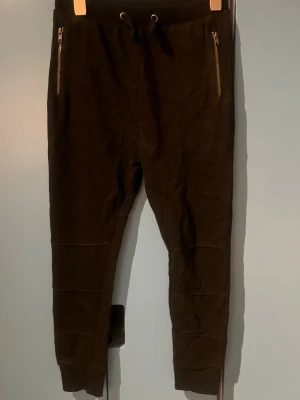 Svarta mjukisbyxor med dragkedjor - Svarta mjukisbyxor med snörning i midjan och dragkedjor på fickorna framtill. Byxorna har två bakfickor och är tillverkade i ett mjukt material som känns skönt mot huden. Perfekta för en avslappnad och chill stil.