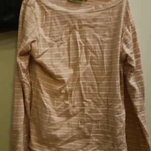 Randig långärmad tröja Indiska M - Ljusrosa och vit randig långärmad tröja från Indiska i storlek M. Tröjan har en klassisk rund halsringning och är gjord i mjuk bomull, perfekt för en chill och avslappnad stil. Passar lika bra till jeans som till kjol.