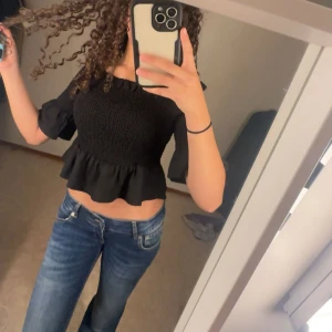 Blå bootcut jeans med låg midja - Säljer ett par snygga blå jeans med bootcut-modell och låg midja. Jeansen har klassiska fickor fram och bak, samt ljusa slitningar för en cool look. Perfekta för dig som gillar en avslappnad och trendig stil. Säljer även tröjan den svarta tröjan från Gina i jätte bra skick 