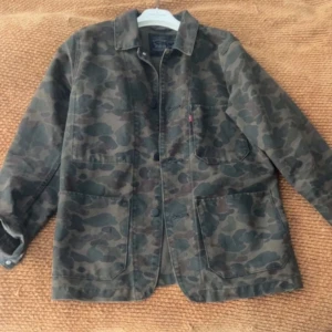 Camouflage overshirt från Levi's - Säljer en snygg overshirt från Levi's i mörkgrönt och brunt camouflage-mönster. Jackan har klassisk krage, stora fickor framtill och knappar längs hela framsidan.  Passar till väldigt mycket och flera olika stilar 