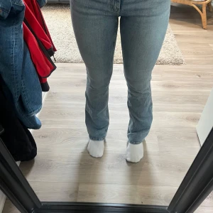 Blå bootcut jeans med hög midja - Säljer ett par klassiska blå jeans med bootcut-snitt och hög midja. Jeansen har en ljus tvätt och raka bakfickor, tillverkade i mjukt denimtyg. Perfekta för dig som gillar en tidlös och avslappnad look.
