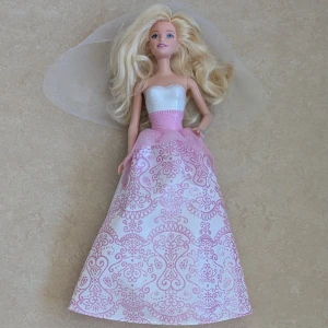 Barbie med jätte fin långkjol och slöja - Barbie med superfin långkjol i vitt och ljusrosa med glittrigt mönster. Barbie bär en slöja . Barbie-bröllop eller bal. Skor till Barbie medföljer inte.