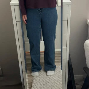 Blå raka jeans med hög midja - Säljer ett par klassiska blå jeans med hög midja och raka ben. Jeansen har en enkel design med fem fickor och stängs med dragkedja och knapp. Perfekta för dig som gillar en tidlös och avslappnad stil.