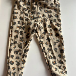 Leopardmönstrade leggings från Minimarket - Beiga leggings från Minimarket med coolt leopardmönster i svart och brunt. Mjukt bomullsmaterial och elastisk midja för skön passform. Perfekta för dig som gillar djurmönster och vill sticka ut lite extra.