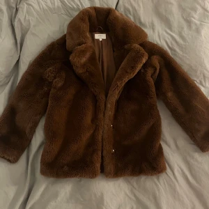 Brun pälsjacka från NA-KD  - Säljer en fluffig brun pälsjacka från NA-KD x dsTara i storlek 36. Jackan har bred krage, dolda tryckknappar och är helfodrad. Perfekt för dig som vill ha en mysig och trendig look under kyliga dagar.