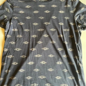 Mörkblå mönstrad t-shirt Jack & Jones - Snygg mörkblå t-shirt från Jack & Jones Vintage Clothing med unikt mönster i beige. Klassisk rund hals och korta ärmar. Tillverkad i mjuk bomull som är skön mot huden. Perfekt för dig som gillar en avslappnad men ändå cool stil.