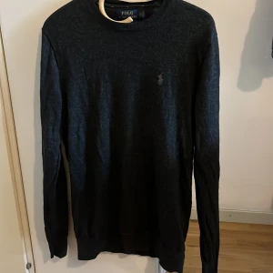 Svart merinoullströja Polo Ralph Lauren - Mörkgrå långärmad tröja från Polo Ralph Lauren i slim fit. Tillverkad i mjuk och tvättbar merinoull med klassisk rund halsringning och diskret broderad logga på bröstet. Perfekt för dig som gillar stilren och enkel design.