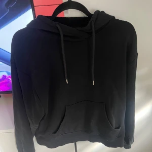 Svart hoodie från Lindex, S - En svart hoodie från Lindex med klassisk känguruficka och snörning i huvan. Tröjan har en relaxed passform och långa ärmar, perfekt för chill dagar. Mjuk insida och enkel stil som funkar till det mesta.