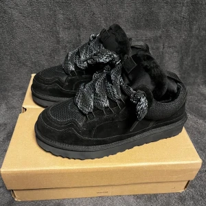 Svarta sneakers UGG Lowmel strl 42 - Säljer ett par svarta UGG Lowmel sneakers med chunky sula och breda snören. Skorna har en mix av mocka och mesh, samt mjuk pälsdetalj runt öppningen. Grymt sköna och snygga till streetwear. Extra svarta skosnören medföljer.