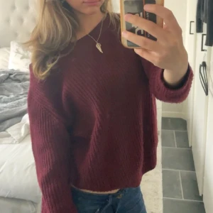 Vinröd stickad tröja med loose fit - Mysig vinröd stickad tröja med loose passform och långa ärmar. Tröjan har en lätt croppad längd och kan bäras offshoulder för en avslappnad vibe. Perfekt till jeans och smycken för en chill look.