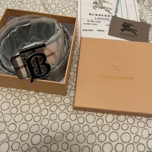 Burberry bälte med klassiskt rutmönster - Säljer ett Burberry bälte i skinn med ikoniskt rutmönster och stor metallspänne med 'B'-logga. Bältet har beige, svart och rosa toner samt detaljer med Burberry-ryttaren. Kommer i originalask med certifikat.