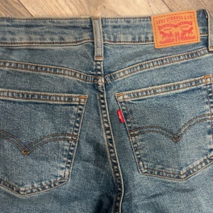 Levi's Superlow Bootcut jeans blå 25 - Säljer ett par Levi's Superlow Bootcut jeans i blå denim. Jeansen har låg midja, är bootcut och har ett hål på ena benet. Typisk Levi's-lapp bak och röda loggan på fickan. Den är väldigt stretchig och skön så den passar både xs och s❤️ 