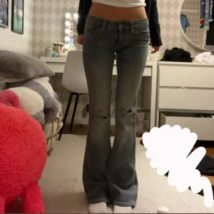 Bootcut jeans från Cheap Monday - Säljer ett par gråblå bootcut jeans från Cheap Monday i storlek 27/32. Jeansen har låg midja, slitna detaljer vid knäna och klassisk femficksdesign. Materialet är mestadels bomull med lite stretch för skön passform.