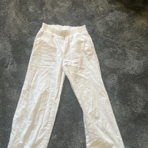 Vita linnebyxor med resårmidja - Snygga vita linnebyxor från C med avslappnad passform och elastisk midja. Byxorna har raka ben och sidfickor, perfekta för en chill och stilren look. Lätta och luftiga i materialet, passar grymt till sommaren.