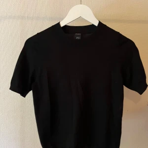 Svart t-shirt från Lindex - En klassisk svart t-shirt från Lindex med rund hals och korta ärmar. Enkel och stilren modell i mjuk bomull, perfekt till jeans eller kjol. Passformen är normal och materialet känns skönt mot huden.