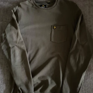 Grön långärmad tröja Lyle & Scott - Snygg olivgrön långärmad tröja från Lyle & Scott med klassisk rund halsringning och bröstficka. Tröjan är i mjuk bomull och passar perfekt till alla tillfällen. Hör av er vid frågor eller prisförslag.😊