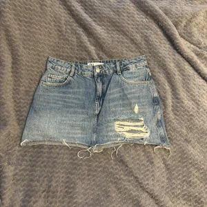Blå jeanskjol med slitningar från Zara - Säljer en blå jeanskjol från Zara i klassisk denim med slitna detaljer och fransig nederkant. Perfekt för dig som gillar en avslappnad och trendig look. Den har tyvärr blivit för liten för mig💞.                           Midja: 39,5cm                                                           Längd: 35cm                                                          