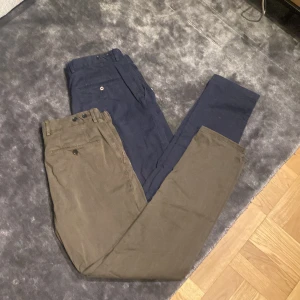 Chinos från Oscar Jacobson, marinblå & khaki - Två par chinos från Oscar Jacobson, ett par i marinblått och ett i khaki. Klassisk rak passform med bälteshällor, knapp och dragkedja. Tillverkade i mjuk bomull, perfekta för en clean och stilren look. Jag säljer dem antingen separat eller begge samtidigt. Styckpris: 350kr  båda: 600kr           Tveka inte med frågor om vad som helst🙌🏽🙌🏽🙌🏽