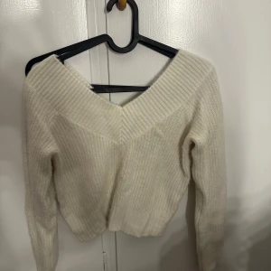 Vit stickad tröja med v-ringning H&M - Supermysig vit stickad tröja från H&M med bred v-ringning och ribbade detaljer. Tröjan har lång ärm och en lite croppad passform som ger en trendig look. Perfekt att styla med jeans eller kjol för en chill vibe.