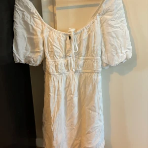 Vit kortklänning med puffärmar - Superfin vit kortklänning med puffiga kortärmar och söt snörning framtill. Klänningen har en luftig passform och är perfekt för varma dagar eller till hösten med boots och skinnjacka.