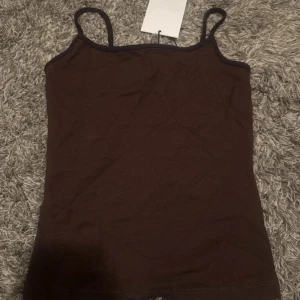 Brun linnetopp från Bershka - Säljer en brun linnetopp från Bershka i storlek S mer som xs skulle jag säga . Toppen har smala axelband och är figurnära med enkel design. Perfekt att styla med jeans eller kjol. Materialet är mjukt och stretchigt, vilket gör den bekväm att bära hela dagen.