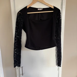 Svart topp med spetsärmar från Nelly - Snygg svart topp från Nelly med spets. Toppen har en fyrkantig ringning och elegant.