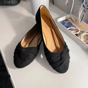 Svarta ballerinaskor  - Säljer ett par svarta ballerinaskor från Graceland med snygg twistad detalj framtill. De är andvända en gång och i superbra skick. Skorna har rund tå, platt sula och är gjorda i mockaliknande syntetmaterial. Perfekta att slänga på sig till jeans eller klänning för en clean look. Bara att dm:a vid frågor eller funderingar!💕