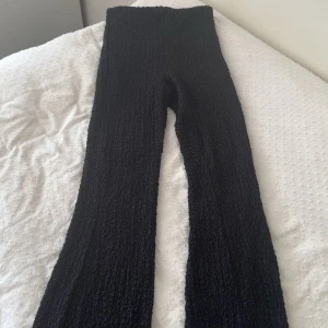 Svarta ribbade byxor från Gina Tricot - Svarta ribbade byxor från Gina Tricot i storlek XS. Byxorna har hög midja och är i ett stretchigt, stickat material som sitter tajt upptill och släpper ut mot benen. Perfekta för en trendig och bekväm look.