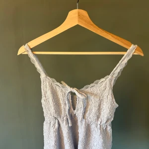 Ljusblå spetsdetaljerad linnetopp - Söt ljusblå linnetopp med smala axelband och spetsdetaljer längs kanterna. Toppen har en knytning framtill och är tillverkad i ett lätt, strukturerat material som känns luftigt och somrigt.