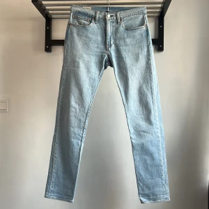 Levi's ljusblå jeans - Ljusblå klassiska Levi's jeans. Jeansen har den ikoniska röda Levi's-taggen på bakfickan och läderpatch i midjan. Tillverkade i slitstarkt denim med knappgylf och normal midja. Storleken 31/34