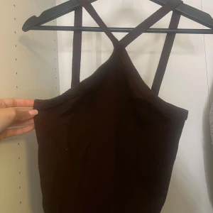 Brun ribbad linnetopp Gina Tricot - Säljer en brun ribbad linnetopp från Gina Tricot i storlek S. Toppen har smala axelband som korsas i ryggen och är ärmlös med en tight passform. Perfekt att styla med jeans eller kjol för en trendig look.