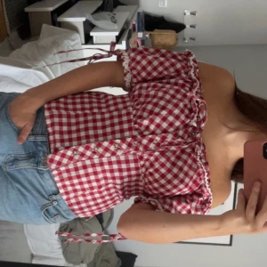 Rutig offshoulder blus med knyt - Supersöt rödvit rutig blus med offshoulder och korta puffärmar. Blusen har knytband vid ärmarna, passar vardags men också fest