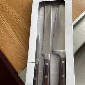 Köksknivar - Detta är ett set med tre köksknivar i originalförpackning. Knivarna har rostfria blad och handtag med nitar. Förpackningen har en mindre reva, men knivarna ser oanvända ut. Perfekt för matlagning och bakning. Ingen elektronik eller digital funktionalitet.