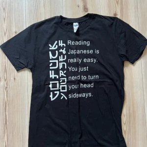 Svart t-shirt med tryck från Gildan - L - Svart t-shirt från Gildan med ett stort vitt tryck på framsidan där det står 'Reading Japanese is really easy. You just need to turn your head sideways.' Trycket har en rolig och edgy design. Klassisk passform och rund hals. Tillverkad i mjuk bomull.