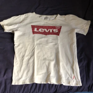 Vit Levi's t-shirt med rött tryck - Vit t-shirt från Levi's med det klassiska röda logotrycket framtill. T-shirten har rund halsringning och korta ärmar. Tillverkad i mjuk bomull, perfekt för en avslappnad och cool stil.