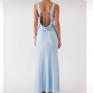 Peppermayo klänning  - Supersnygg ljusblå långklänning i satinliknande material med öppen rygg och snörning. Klänningen har smala axelband, draperad urringning och figurnära passform. Perfekt för dig som vill sticka ut med en elegant och trendig look.