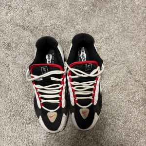 Nike Air Max Triax 96 - Nike Air Max Triax 96 sneakers i svart, vitt och rött. Skorna har en klassisk retrodesign med vit sula, svarta meshpaneler och vita samt röda detaljer. Swoosh-logga på sidan och framtill, samt snörning med röda öglor. Perfekta för dig som gillar old school vibes.