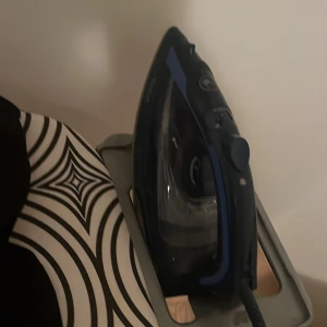 Ångstrykjärn - Strykjärn med ångfunktion i svart och blå design. Synlig vattentank och vred för temperaturinställning. Ser ut att vara i gott skick utan synliga skador eller slitage. Perfekt för att hålla kläder släta och fräscha.