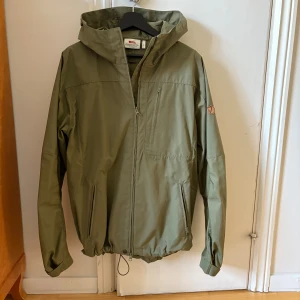 Vindjacka Sten Jacket från Fjällräven  - Vattenavvisande höst/vårjacka. Fast huva med två handfickor och en bröstficka. Jackan kan vaxas för skydd mot vind och väta. Slitstark! 