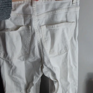 Vita raka jeans med dragkedja - Säljer ett par vita jeans med klassisk femficksdesign och raka ben. Byxorna har dragkedja och knapp framtill samt bälteshällor. Materialet är kraftig bomull med jeansstruktur. Perfekta för en clean och fräsch look.