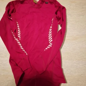 Rosa långärmad träningströja Helly Hansen - Säljer en rosa långärmad träningströja från Helly Hansen med vita diagonala ränder på sidorna. Tillverkad i 100% polypropylen, perfekt för aktiva dagar. Tröjan har en sportig look och är superlätt och smidig att bära.