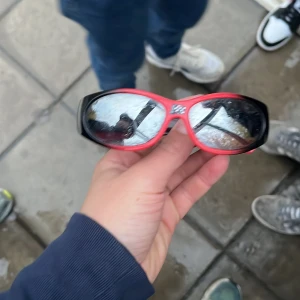 Röda och svarta Cars solglasögon - Säljer ett par coola solglasögon med röd och svart båge och spegelglas. På sidan finns en bild på Lightning McQueen från Cars. Glasögonen har en sportig, oval form och passar perfekt för dig som gillar att sticka ut med din stil.