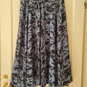 Mönstrad långkjol strl 5XL - Snygg långkjol i blått och svart med abstrakt mönster. Kjolen har resår i midjan och ett knytband framtill. Tillverkad i 100% polyester. Hela längden: 86cm. Storlek 5XL.