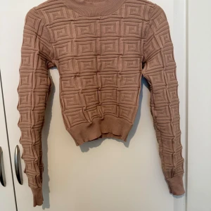 Beige stickad tröja med 3D-mönster - Säljer en beige stickad tröja med unikt 3D-mönster i rutigt labyrintmönster. Tröjan har rund halsringning, ribbade muddar och lång ärm. Perfekt för dig som vill ha något annorlunda och trendigt i garderoben.