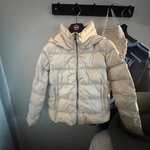 Beige pufferjacka från Colmar - Snygg beige pufferjacka från Colmar med huva och dragkedja framtill. Jackan har en quiltad look och rund Colmar-logga på ärmen. Perfekt för kalla dagar och ger en clean vibe till din outfit. Nypris 5000kr. Skriv om ni har frågor!💕storlek ca 158 men skulle säga att det är en xxs-xs