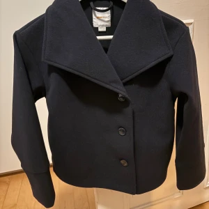 Mörkblå kavajjacka från Gina Tricot - Stilren mörkblå kavajjacka från Gina Tricot med bred krage och tre knappar framtill. Jackan har en rak passform och är helfärgad utan mönster. Använd 1 gång! Så mycket fint skick.